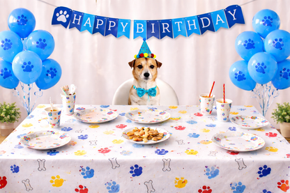 Dog celebrating a birthday with a 'Happy Birthday' banner, balloons, and a table set with plates and food.